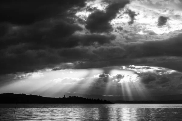 Sunrays at near sunset, with dark clouds in the background, above Trasimeno lake, Umbria, Italy.