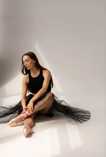 Prachtige ballerina zittend op de vloer en aangrijpende benen. — Stockfoto