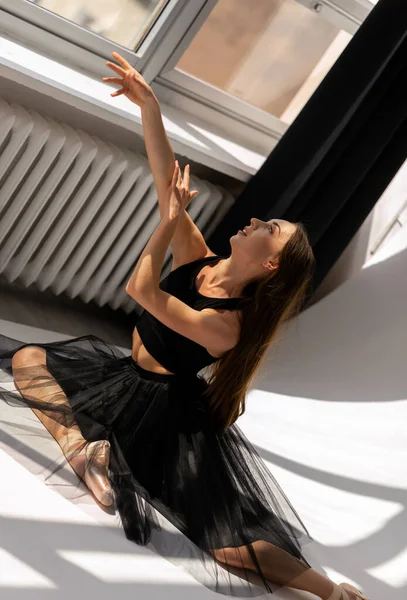 Ballerina in zwarte jurk zittend op de vloer dansend met licht. — Stockfoto