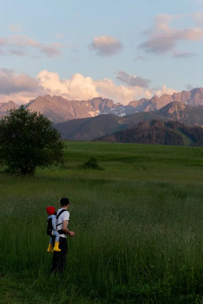 Babası, Polonya Dağları 'ndaki Zakopane yakınlarındaki bir dağda küçük bir çocukla birlikte askısında ya da sırt çantasında yürüyordu. Yaz günbatımı Carpathian Hills dağlarında ve yol yeşil çimlerin arasında. Doğa arkaplanı.