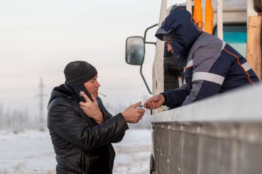 Kapüşonlu ve siyah örgülü şapkalı cep telefonuyla konuşan bir montajcının portresi.