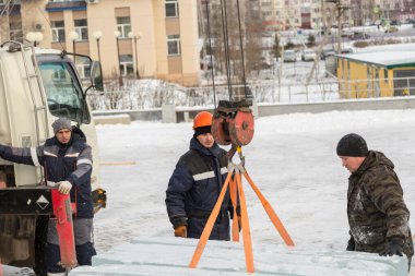 Üç montaj işçisi bir arabanın gövdesinden buz kalıpları boşaltıyor.