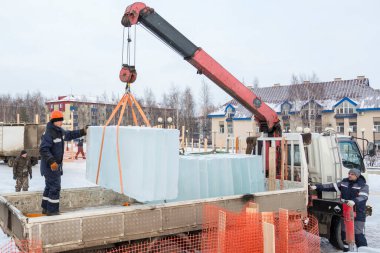 Üç montaj işçisi bir arabanın gövdesinden buz kalıpları boşaltıyor.