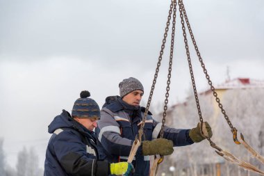 İki montaj işçisi bir arabanın gövdesinden buz kalıplarını boşaltıyor.