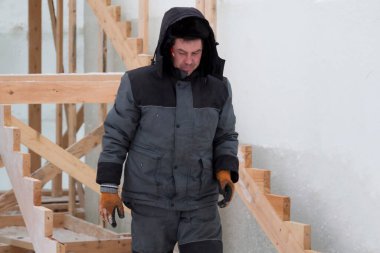 Mavi ceketli bir montajcı ahşap kirişlerden yapılmış bir kaydırağın çerçevesini monte eder.