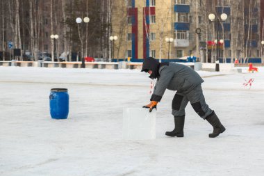 A worker in winter overalls pushes an ice block along the construction site of an ice town clipart