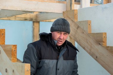 Mavi ceketli bir montajcı ahşap kirişlerden yapılmış bir kaydırağın çerçevesini monte eder.