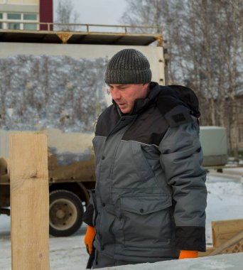 Mavi ceketli bir montajcı ahşap kirişlerden yapılmış bir kaydırağın çerçevesini monte eder.