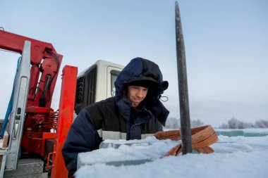 Mavi ceketli ve buz panelinin yanında örülmüş siyah şapkalı bir montajcının portresi.