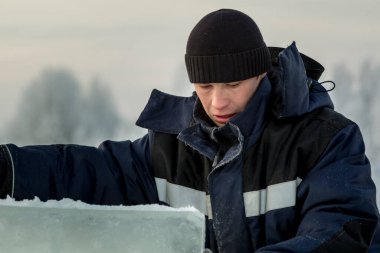 Mavi ceketli ve buz panelinin yanında örülmüş siyah şapkalı bir montajcının portresi.