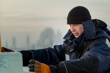 Mavi ceketli ve buz panelinin yanında örülmüş siyah şapkalı bir montajcının portresi.