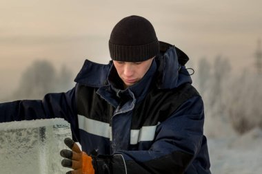 Mavi ceketli ve buz panelinin yanında örülmüş siyah şapkalı bir montajcının portresi.