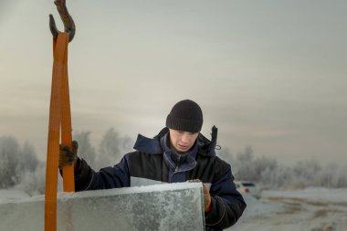 Ceketli ve siyah şapkalı işçi derleyicisi buz bloklarını boşaltıyor