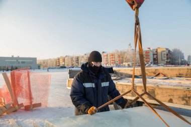Ceketli ve siyah şapkalı işçi derleyicisi buz bloklarını boşaltıyor