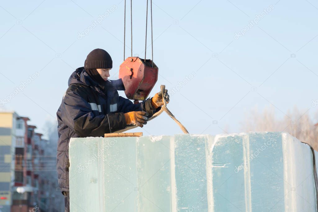 Worker assembler in jacket and black hat unloads ice blocks