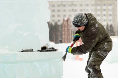 Heykeltıraş buz kalıbından bir buz parçasını keskiyle döver.