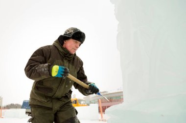 Heykeltıraş buz kalıbından bir buz parçasını keskiyle döver.