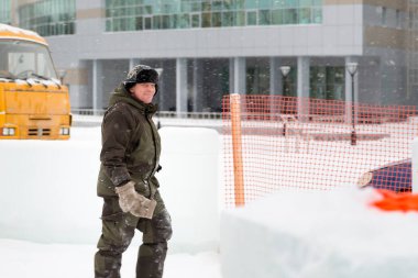 Kış üniformalı bir işçi, buz kasabasının inşaat alanında yürüyor.