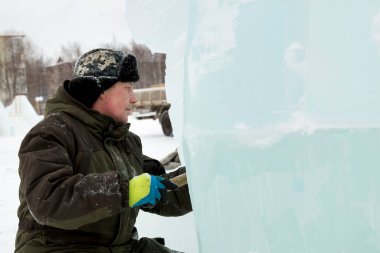 Heykeltıraş buz kalıbından bir buz parçasını keskiyle döver.