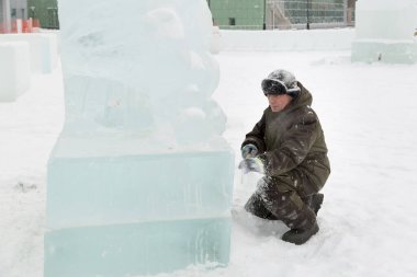 Heykeltıraş buz kalıbından bir buz parçasını keskiyle döver.