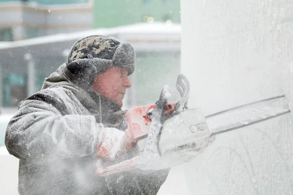 The sculptor cuts an ice figure out of ice by a chainsaw for Christmas