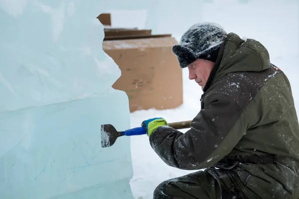 stock image The sculptor beats off a piece of ice from an ice block with a chisel