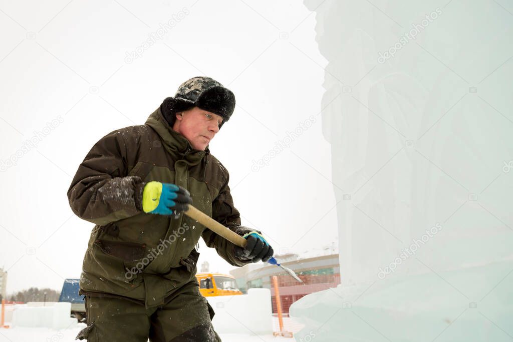 The sculptor beats off a piece of ice from an ice block with a chisel