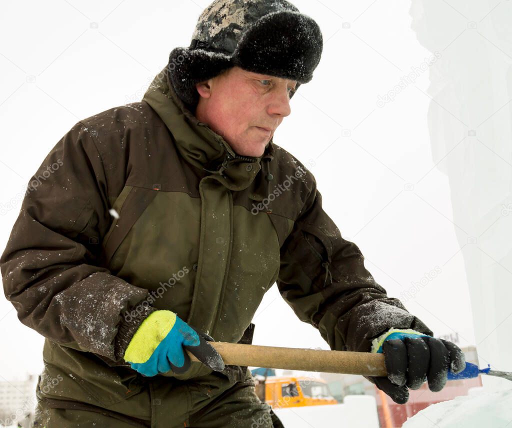 The sculptor beats off a piece of ice from an ice block with a chisel