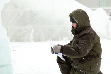 Yeşil kapüşonlu ceketli bir işçi bir kağıt parçasındaki diyagramı inceliyor.