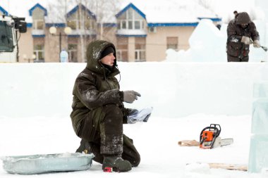 Yeşil kapüşonlu ceketli bir işçi bir kağıt parçasındaki diyagramı inceliyor.