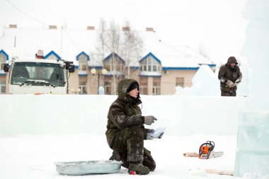 Yeşil kapüşonlu ceketli bir işçi bir kağıt parçasındaki diyagramı inceliyor.