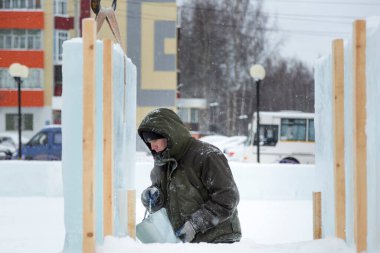 Yeşil kapüşonlu ceketli bir buz kasabası müteahhidi buz kalıbının üzerinden su döker.