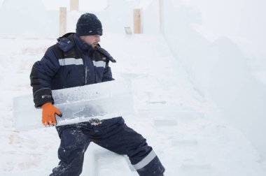 Bir işçi buz kasabası boyunca kollarında bir buz bloğu taşıyor.