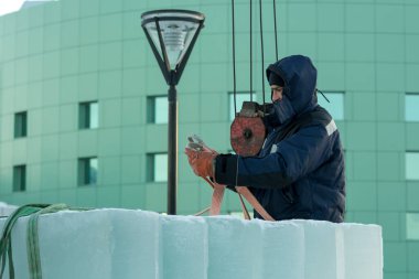 Mavi kapüşonlu ve siyah şapkalı Slinger Derleyicisi buz kalıplarını boşaltıyor.