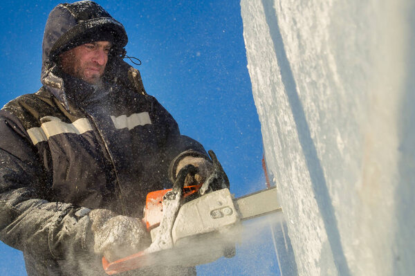 A worker with a chainsaw in his hands on the installation of the ice panel