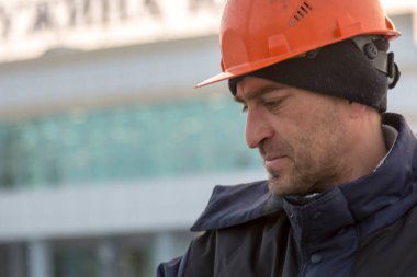 Kafasında siyah örgü şapkalı mavi ceketli bir tesisatçının portresi.