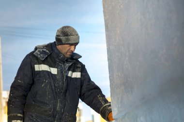 Mavi ceketli ve buz panelinin yanında örülmüş siyah şapkalı bir montajcının portresi.