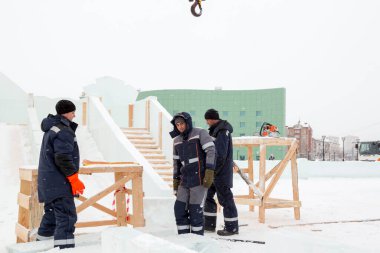 Üç işçi ahşap bir kaydırağın çerçevesini buz panelleriyle kaplıyor.