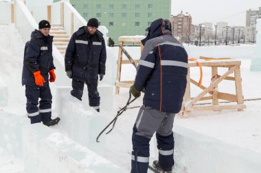 Üç işçi ahşap bir kaydırağın çerçevesini buz panelleriyle kaplıyor.