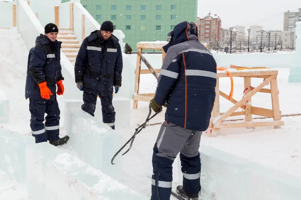 Üç işçi ahşap bir kaydırağın çerçevesini buz panelleriyle kaplıyor.