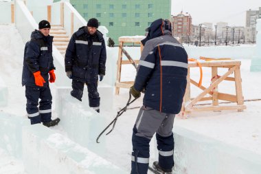 Üç işçi ahşap bir kaydırağın çerçevesini buz panelleriyle kaplıyor.