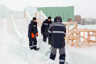 Üç işçi ahşap bir kaydırağın çerçevesini buz panelleriyle kaplıyor.