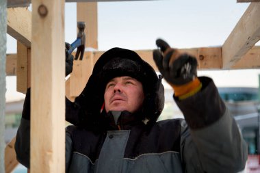 Gri kapüşonlu ceketli, elinde çekiçle ahşap bir strümanın montajında çalışan adam.