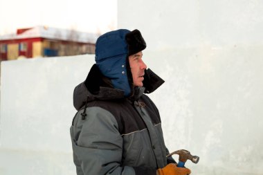 Gri kapüşonlu ceketli, elinde çekiçle ahşap bir strümanın montajında çalışan adam.