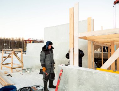 Gri kapüşonlu ceketli, elinde çekiçle ahşap bir strümanın montajında çalışan adam.