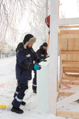 İki işçi, ahşap bir kaydırağın çerçevesini buz panelleriyle kaplıyor.