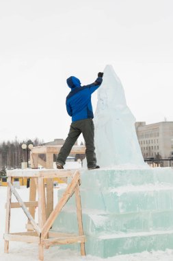 Heykeltıraş, bir buz kalıbından bir buz figürünü kesiyor ve İsa için bir keski ile ahşap bir iskelenin üzerinde duruyor.