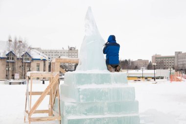 Heykeltıraş, bir buz kalıbından bir buz figürünü kesiyor ve İsa için bir keski ile ahşap bir iskelenin üzerinde duruyor.