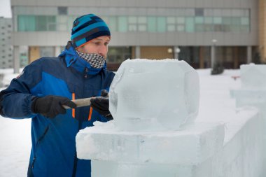 Bir heykeltıraş yontulmuş bir keskiyle buz bloğundan yuvarlak bir buz topu oyuyor..