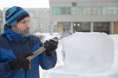 Bir heykeltıraş yontulmuş bir keskiyle buz bloğundan yuvarlak bir buz topu oyuyor..